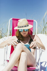 Junge Frau liest ein Buch beim Sonnenbaden am Strand an einem sonnigen Tag - CAVF52445