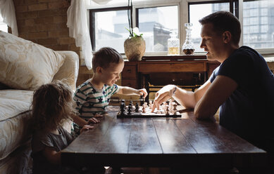 Seitenansicht eines Vaters, der mit seinen Kindern zu Hause am Tisch Schach spielt - CAVF52453