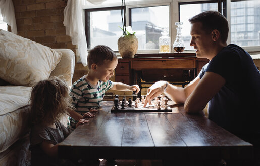 Side view of father playing chess with children on table at home - CAVF52453