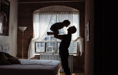 Silhouette Vater, der seine Tochter abholt, während er zu Hause am Bett steht - CAVF52458