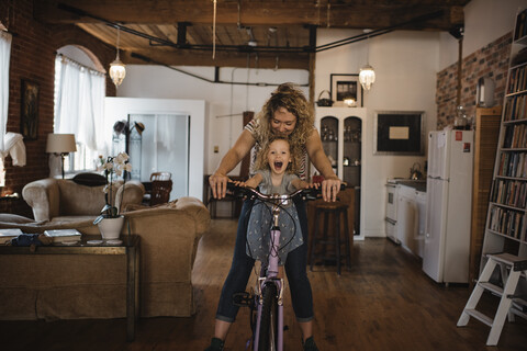 Happy mother with daughter riding bicycle at home stock photo