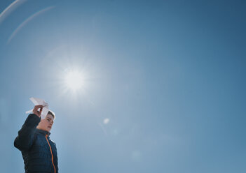 Niedriger Blickwinkel des Jungen hält Papierflugzeug im Stehen gegen klaren blauen Himmel an einem sonnigen Tag - CAVF52528