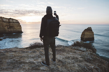 Rückansicht eines Mannes, der ein Selfie mit seinem Handy macht, während er am Strand gegen den Himmel bei Sonnenuntergang steht - CAVF52535
