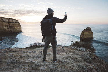 Rückansicht eines Mannes, der ein Selfie mit seinem Smartphone macht, während er am Strand gegen den Himmel bei Sonnenuntergang steht - CAVF52536