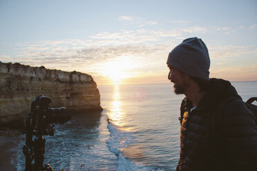 Man with camera standing at beach against sky during sunset - CAVF52547