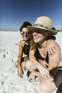 Fröhliche Freundinnen kauern am Strand während eines sonnigen Tages - CAVF52565