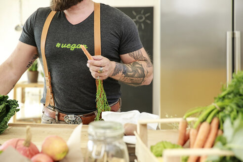 Vegan man holding carrot in his kitchen - REAF00351