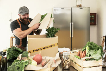 Mature man with delivery service packing organic vegetables in cardboard - REAF00363
