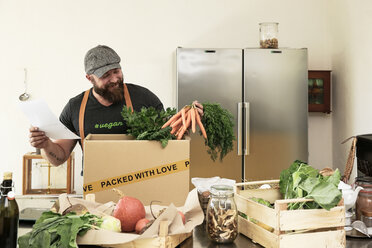 Mature man with delivery service packing organic vegetables in cardboard - REAF00367