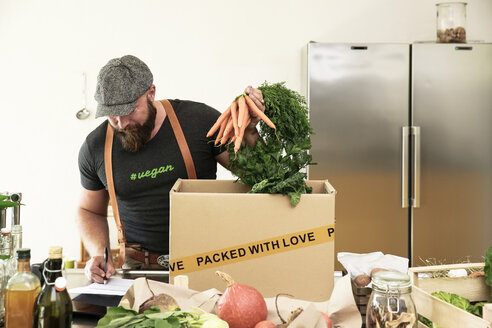 Mature man with delivery service packing organic vegetables in cardboard - REAF00368