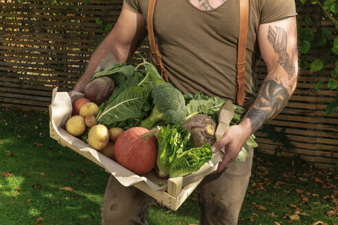 Mature man carrying crate with vegetables in his garden - REAF00387