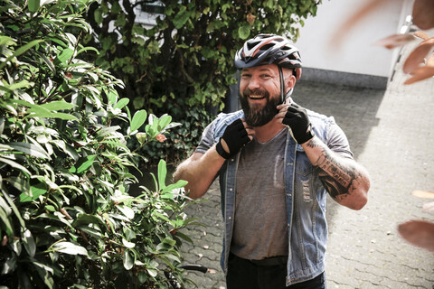 Porträt eines lachenden Mannes, der einen Fahrradhelm aufsetzt, lizenzfreies Stockfoto