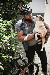 Smiling man with bicycle carrying dog - REAF00401