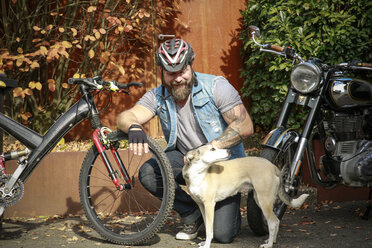 Lächelnder Mann mit Hund zwischen Motorrad und Fahrrad - REAF00419