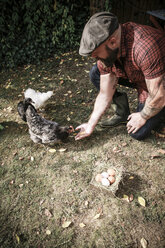 Mann in seinem eigenen Garten, Mann füttert freilaufende Hühner - REAF00431