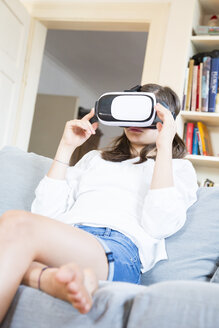 Mädchen sitzt zu Hause auf der Couch und benutzt eine Virtual-Reality-Brille - LVF07517