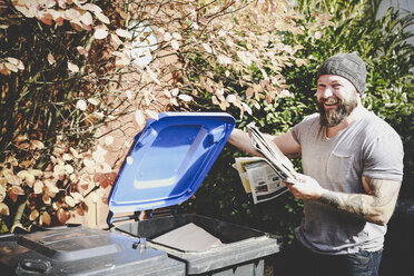 Porträt eines lachenden Mannes, der Altpapier in einer Papierbank recycelt - REAF00450
