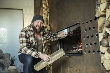 Portrait of bearded man lighting fireplace at home - REAF00455