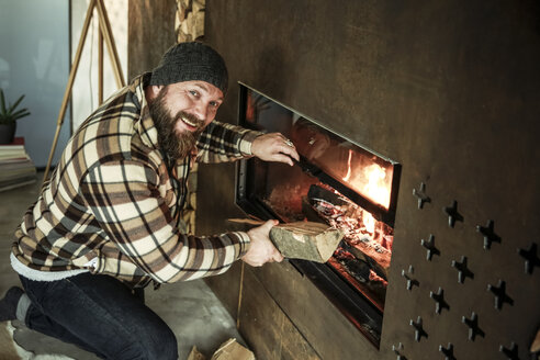 Portrait of bearded man kneeling in front of fireplace at home - REAF00457