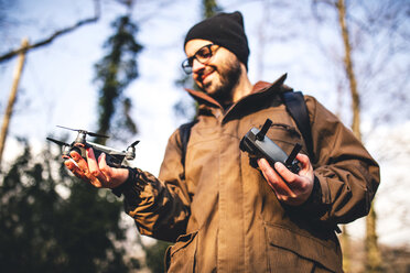 Niedriger Blickwinkel von männlichen Wanderer hält Quadcopter, während gegen den Himmel im Wald stehen - CAVF52646