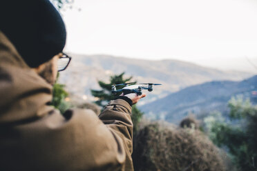 Männlicher Wanderer hält Quadcopter, während er auf einem Berg im Wald steht - CAVF52652