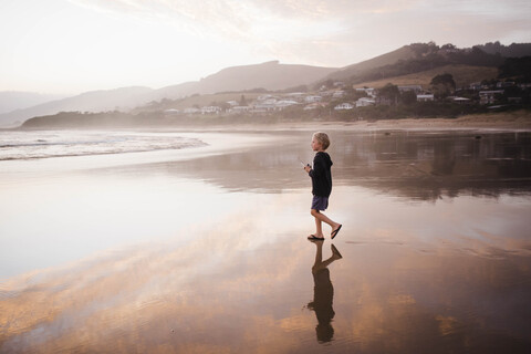 Seitenansicht eines Jungen, der beim Spazierengehen am Strand gegen den Himmel bei Sonnenuntergang wegschaut, lizenzfreies Stockfoto