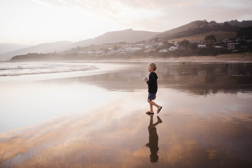 Seitenansicht eines Jungen, der beim Spazierengehen am Strand gegen den Himmel bei Sonnenuntergang wegschaut - CAVF52673