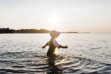 Seitenansicht eines Mädchens, das eine Mütze trägt, während es im Meer gegen den Himmel bei Sonnenuntergang läuft - CAVF52674