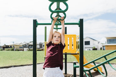 Junge, der auf dem Spielplatz gegen den wolkenverhangenen Himmel am Klettergerüst hängt, an einem sonnigen Tag - CAVF52681