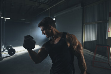 Male athlete lifting dumbbell while standing in gym - CAVF52682