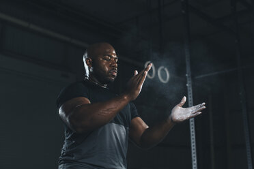 Low angle view of male athlete applying chalk on hands while standing in gym - CAVF52684