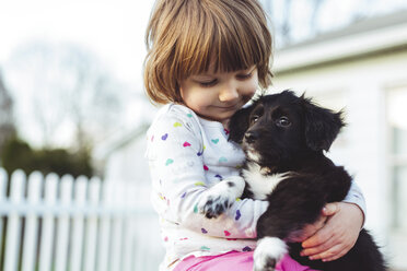 Low angle view of girl carrying puppy while standing at yard - CAVF52691