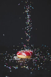 Sprinkles sprinkling on donut at wooden table against black background - CAVF52698