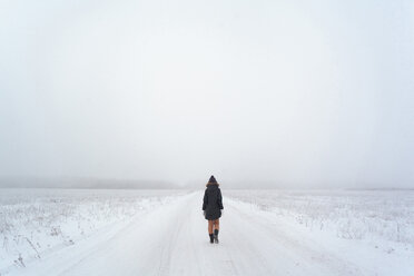 Rear view of woman walking on snowy field against sky during foggy weather - CAVF52739