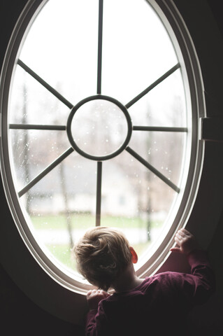 Rückansicht eines kleinen Jungen, der durch ein Fenster zu Hause schaut, lizenzfreies Stockfoto