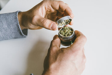 Cropped hands of man grinding marijuana in metallic grinder over table at home - CAVF52777