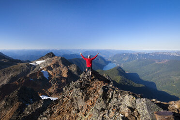 Rückansicht eines Wanderers mit erhobenen Armen, der auf einem Berg vor einem klaren Himmel steht - CAVF52796