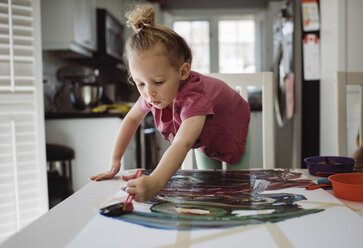 Mädchen malt auf Papier, während sie am Tisch zu Hause steht - CAVF52867