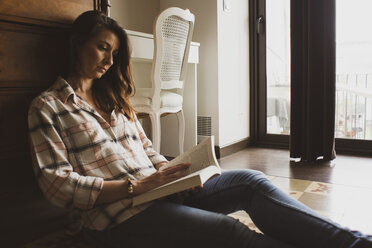 Frau liest ein Buch, während sie zu Hause auf dem Boden sitzt - CAVF52878