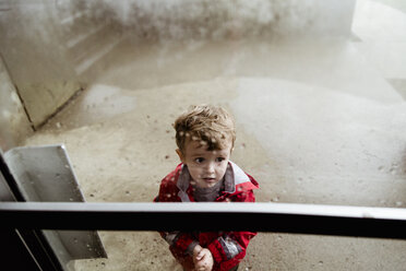 High angle view of cute worried boy wearing raincoat seen through wet window - CAVF52896