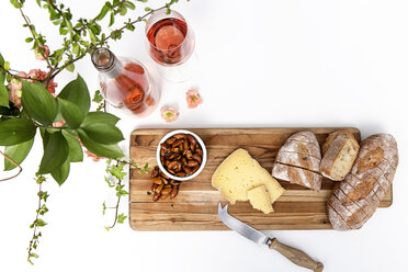 High angle view of bread with cheese and almonds on cutting board by wine over white background - CAVF52915