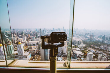 Close-up of coin-operated binoculars by window against cityscape and sky - CAVF52922