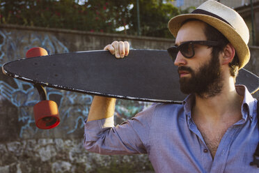 Mann mit Sonnenbrille und Hut, der ein Skateboard an die Wand hält - CAVF52936