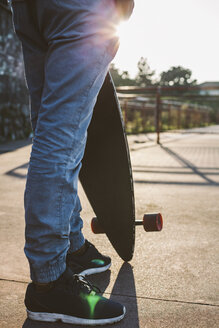 Tiefschnitt eines Mannes, der ein Skateboard hält, während er bei Sonnenuntergang vor dem Himmel steht - CAVF52938