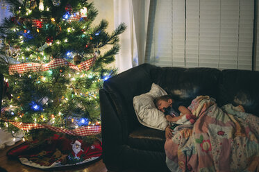 Schlafender Junge auf dem Sofa unter dem beleuchteten Weihnachtsbaum bei Nacht - CAVF52951