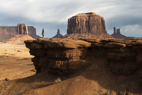 Ansicht einer Frau aus mittlerer Entfernung, die an einer Felsformation im Oljato-Monument Valley steht, lizenzfreies Stockfoto