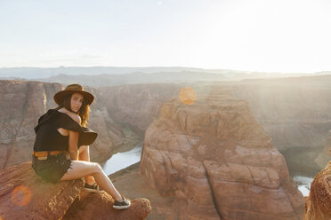 Ganzkörperporträt einer jungen Frau, die auf einem Felsen am Horseshoe Bend in der Wüste sitzt, während eines sonnigen Tages - CAVF52987