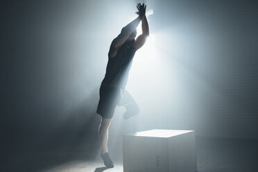 Anpassungsfähiger Sportler mit erhobenen Armen, der in der Turnhalle auf einen Kasten springt - CAVF53009