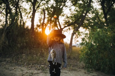 Girl wearing hat while holding fish in forest during sunset - CAVF53025