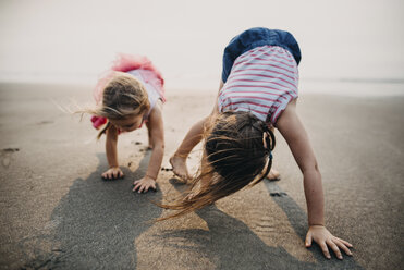 Playful sisters bending on sand at beach against sky - CAVF53053